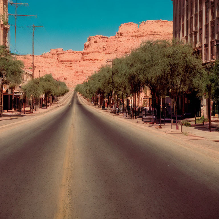 Deserted street with buildings and trees leading to red rock formation