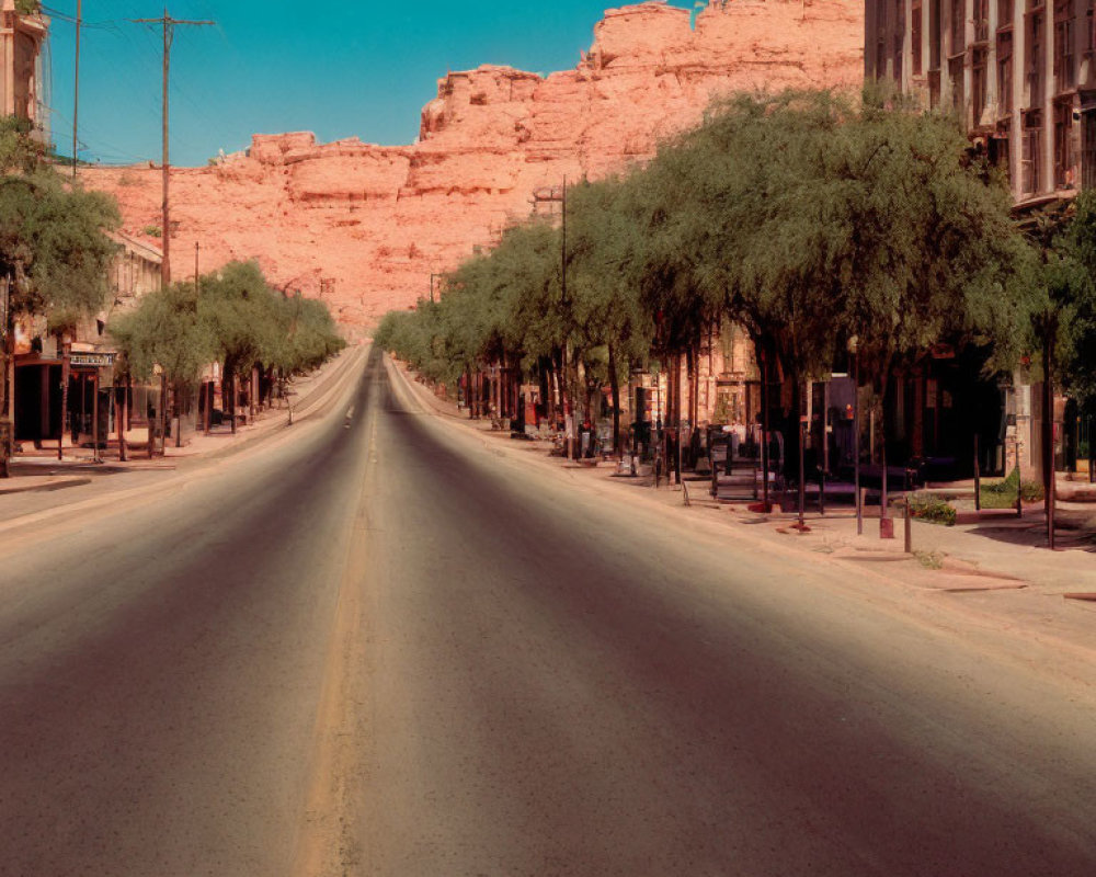 Deserted street with buildings and trees leading to red rock formation