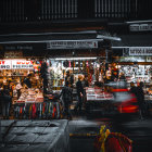 Nighttime street view of a bustling flower shop with warm lights and people browsing floral arrangements.