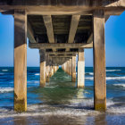 Ocean pier with concrete pillars, waves crashing, blue sky, and distant clouds