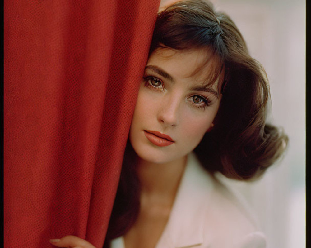 Woman with dark hair and white blouse peeking from red curtain