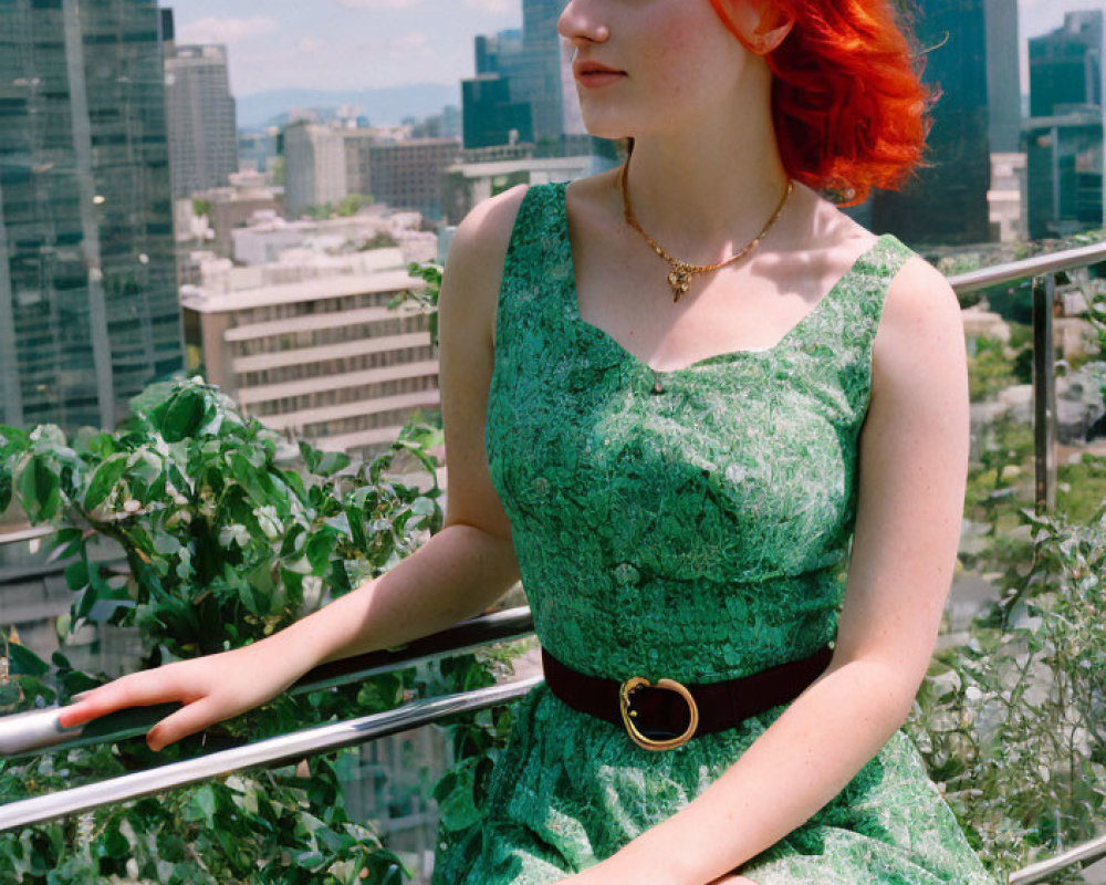 Red-haired woman in green dress sitting on railing with cityscape view.