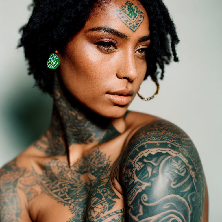 Portrait of woman with intricate tattoos, green earring, and nose ring