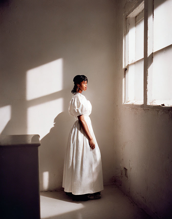 Vintage woman in white dress and hat by window with strong shadows