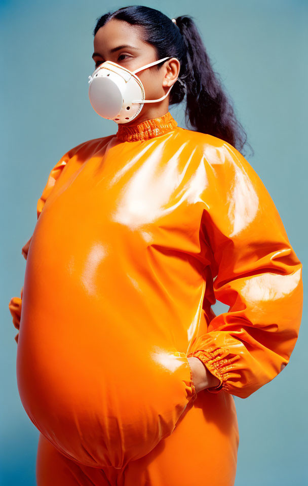 Female in orange protective suit and white mask on blue backdrop