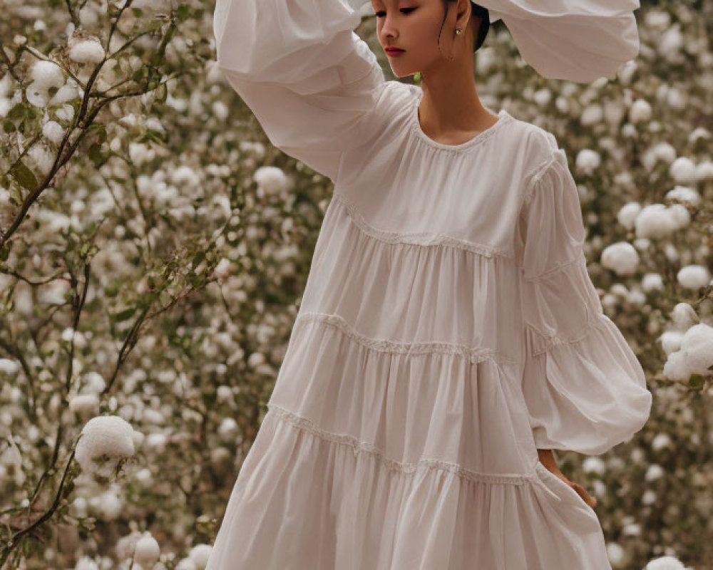 Woman in flowing white dress among fluffy white blooms with oversized sleeves
