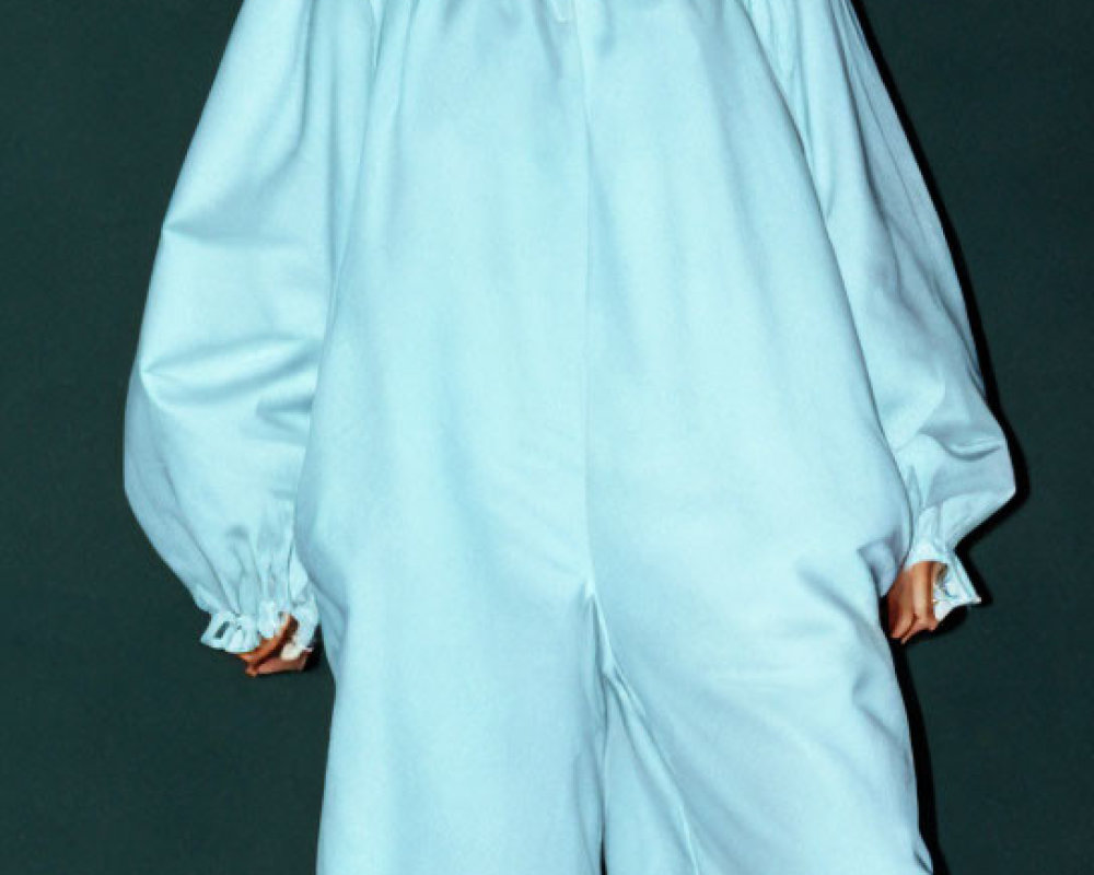 Person in Voluminous Light Blue Garment on Dark Background