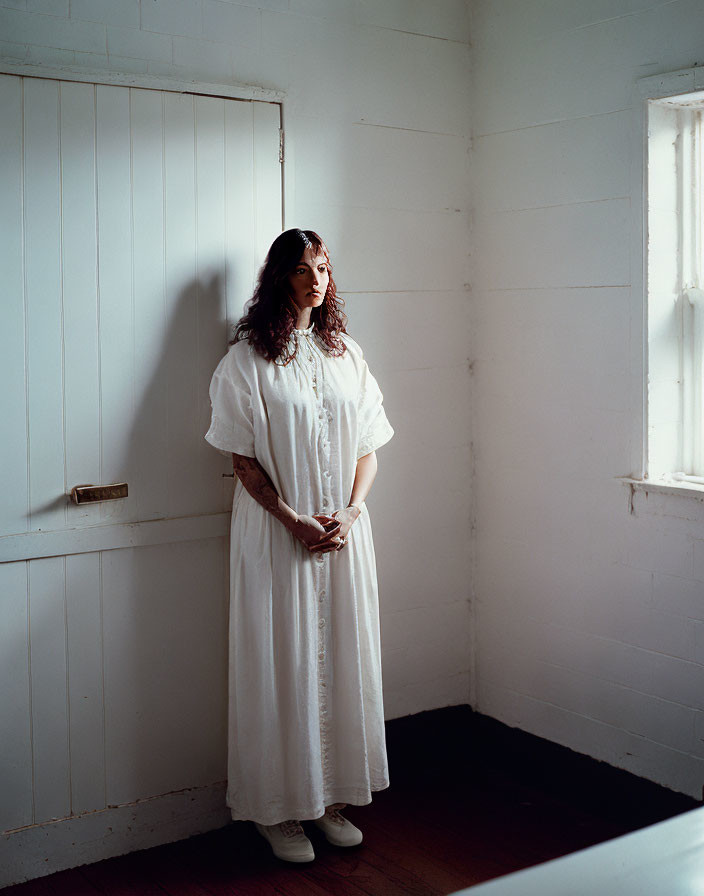 Woman in White Dress Standing in Sparse Room with Wooden Floors and Walls