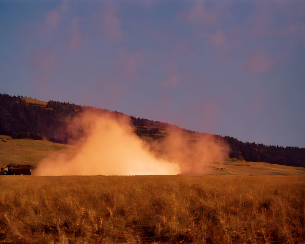 Scenic golden hour lighting on rural landscape with dust cloud and forested hillside