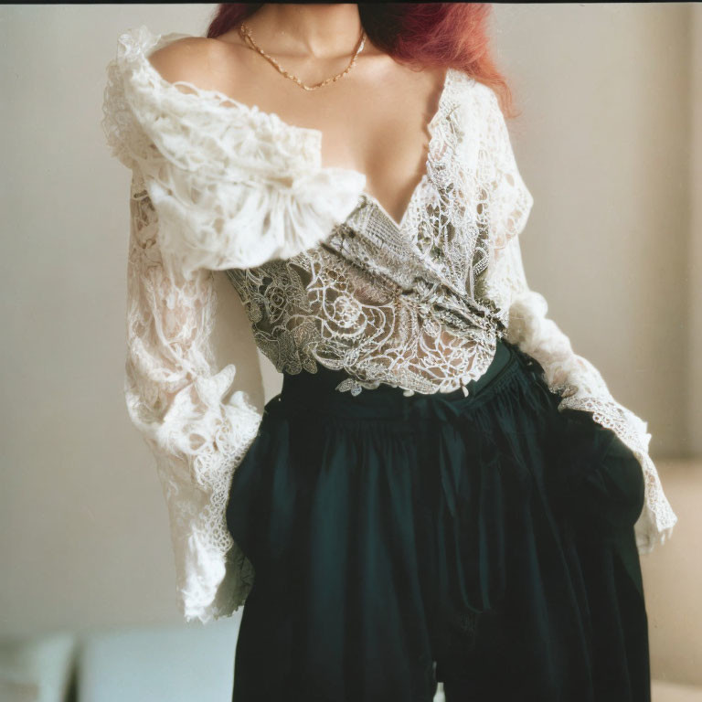 Red-haired person in lace top and black trousers on neutral background