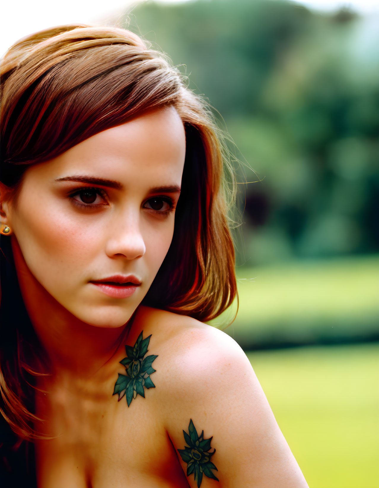Short-haired woman with shoulder tattoos in thoughtful pose on green backdrop.