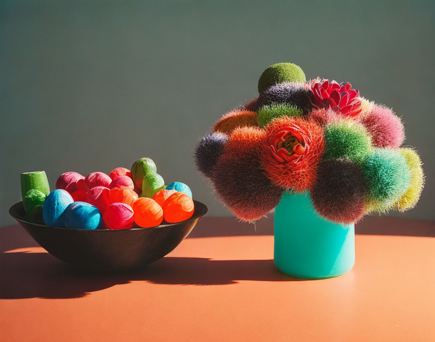 Colorful spherical flowers in teal vase with multicolored balls on coral surface.