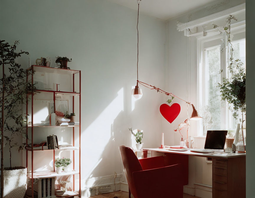 Red chair, desk, heart-shaped lamp in cozy workspace with sunlight and plants