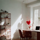 Red chair, desk, heart-shaped lamp in cozy workspace with sunlight and plants