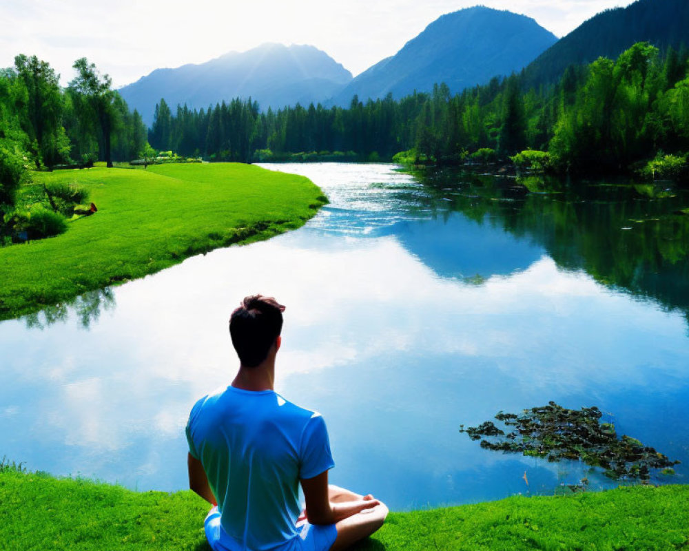 Person in Blue Shirt Relaxing by Serene River amid Lush Greenery