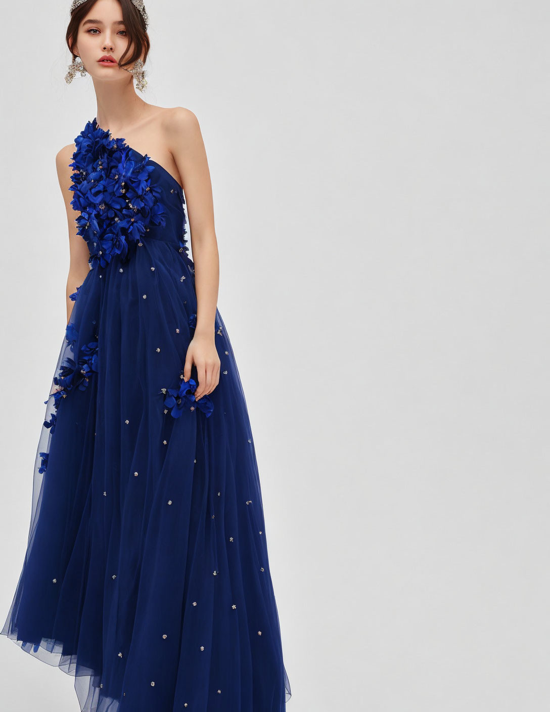Woman in one-shoulder blue gown with floral embellishments on sheer skirt