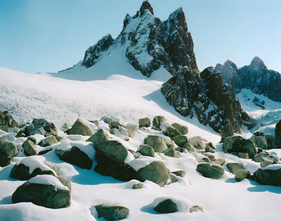 Snow-covered boulders and jagged mountain peak under blue sky