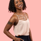 Smiling woman with curly hair in white top and navy bottom on pink background