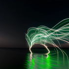 Nighttime light painting creates arched patterns on water.