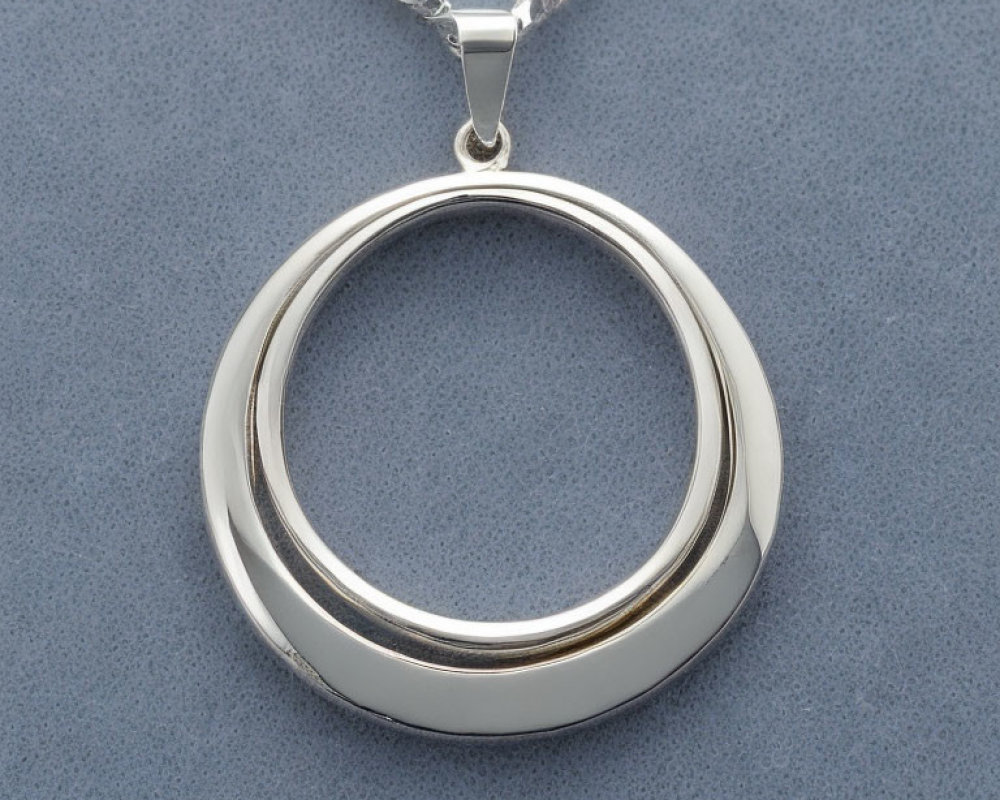 Circular Silver Pendant on Chain Against Gray Background