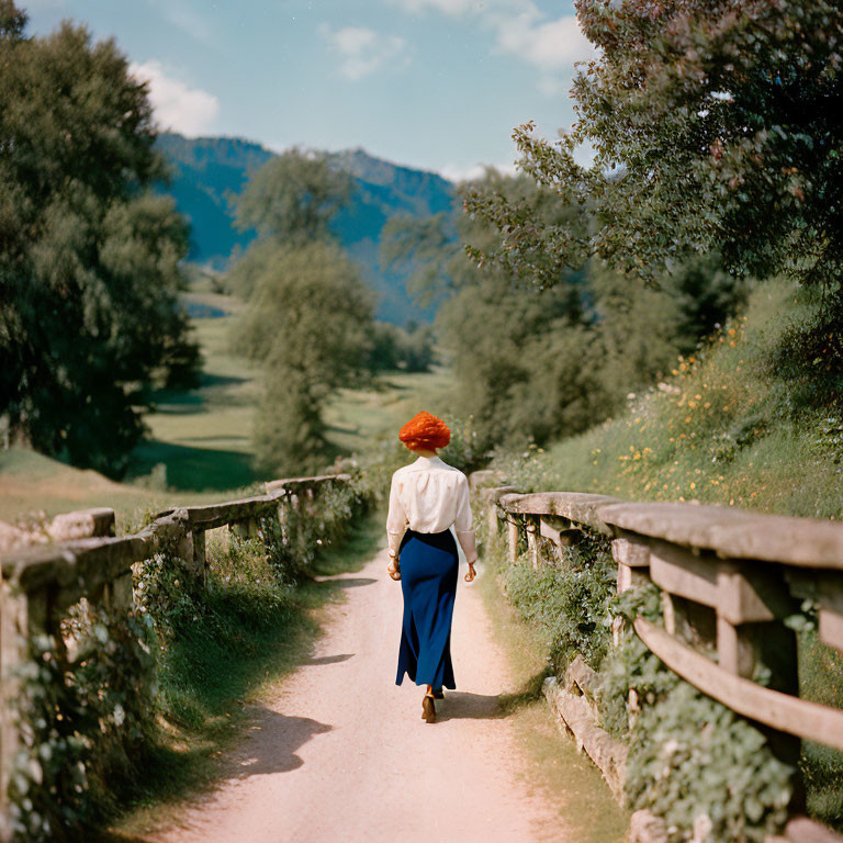 Person in Blue Skirt Walking on Rural Path with Wooden Fences and Green Fields