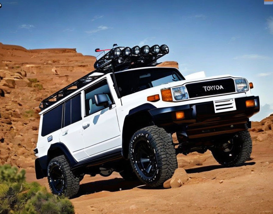 White Toyota off-road SUV with roof rack and extra lights parked in rocky desert under clear blue sky