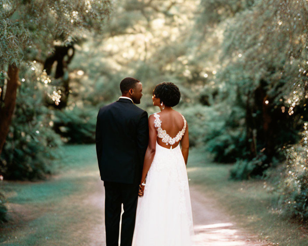 Wedding couple walking down tree-lined path in sunlight