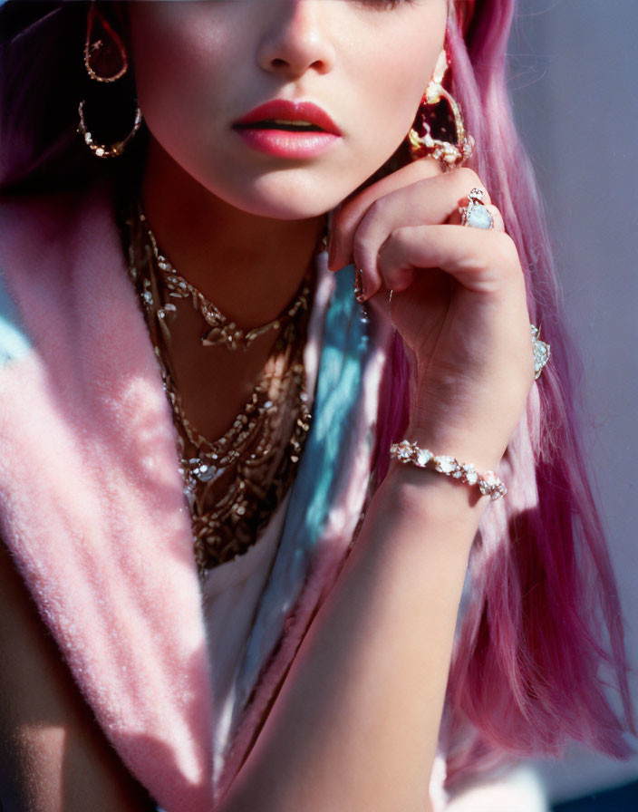 Pink-haired person in pastel fur coat with gold jewelry against soft background.