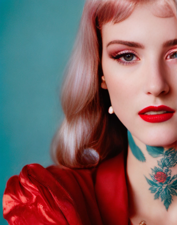Woman with red lip, tattooed neck, dual-toned hair in red outfit against teal backdrop