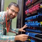 Man in glasses connecting cables on network server with glowing lights