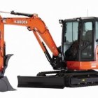 Compact orange mini excavator with metal arm and bucket on treads and clear cabin.