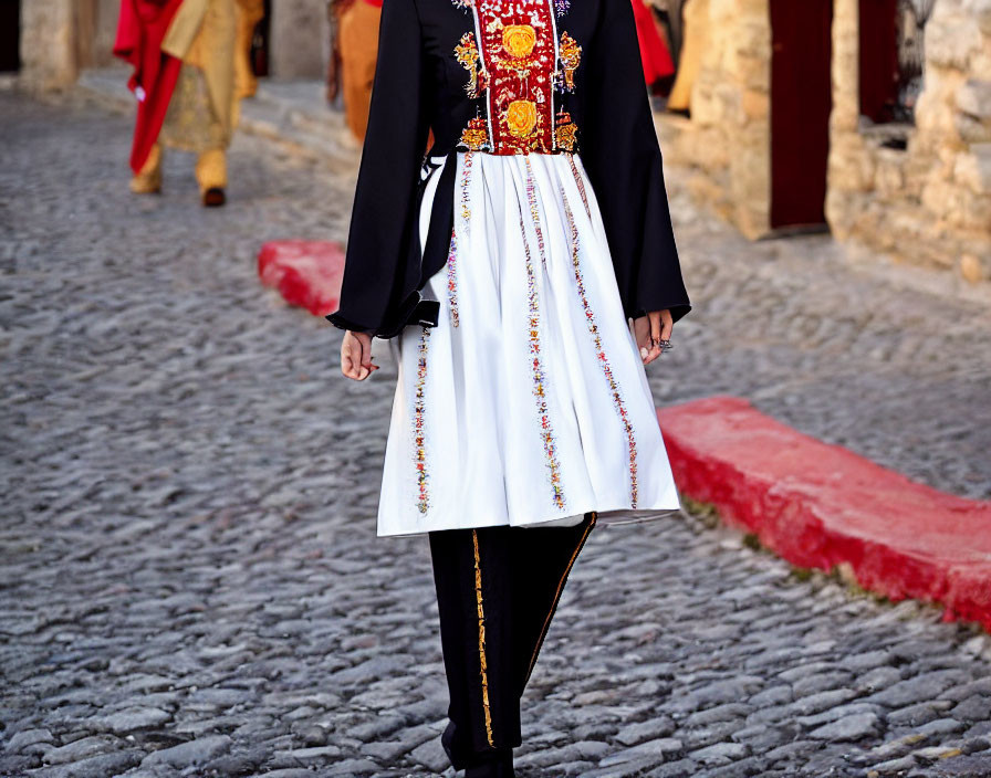 Traditional Costumed Person Walking on Cobblestone Street with Others