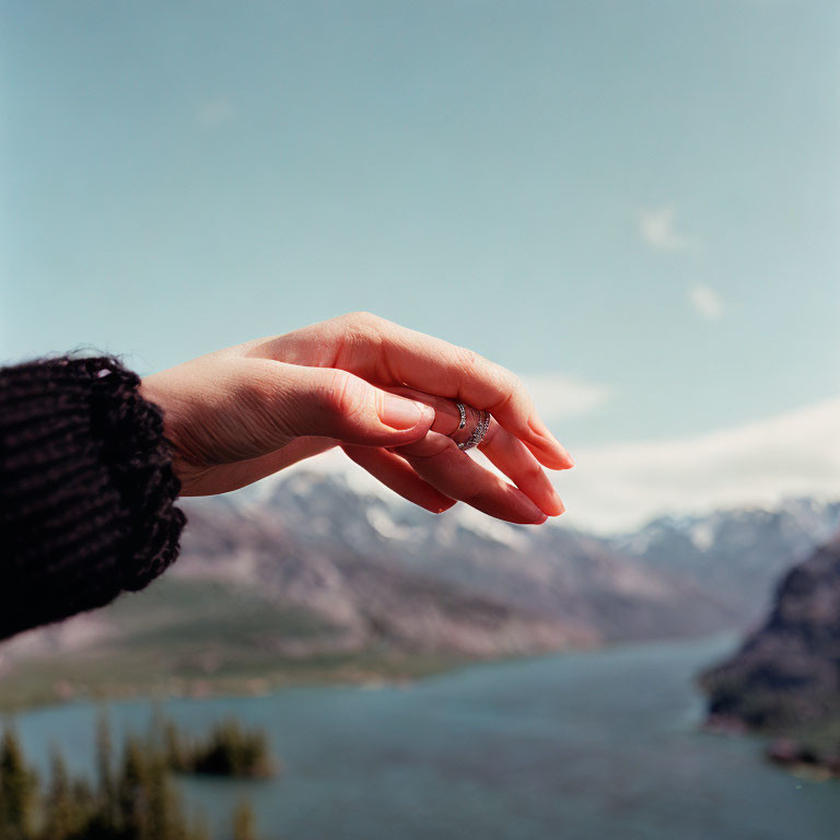 Hand with Ring Gesturing Against Lake and Mountain Backdrop