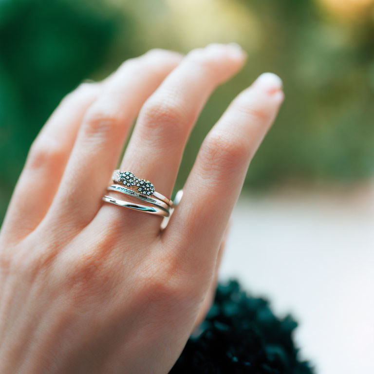 Close-up of hand with stacked rings: silver band & turquoise gemstone on blurred green background