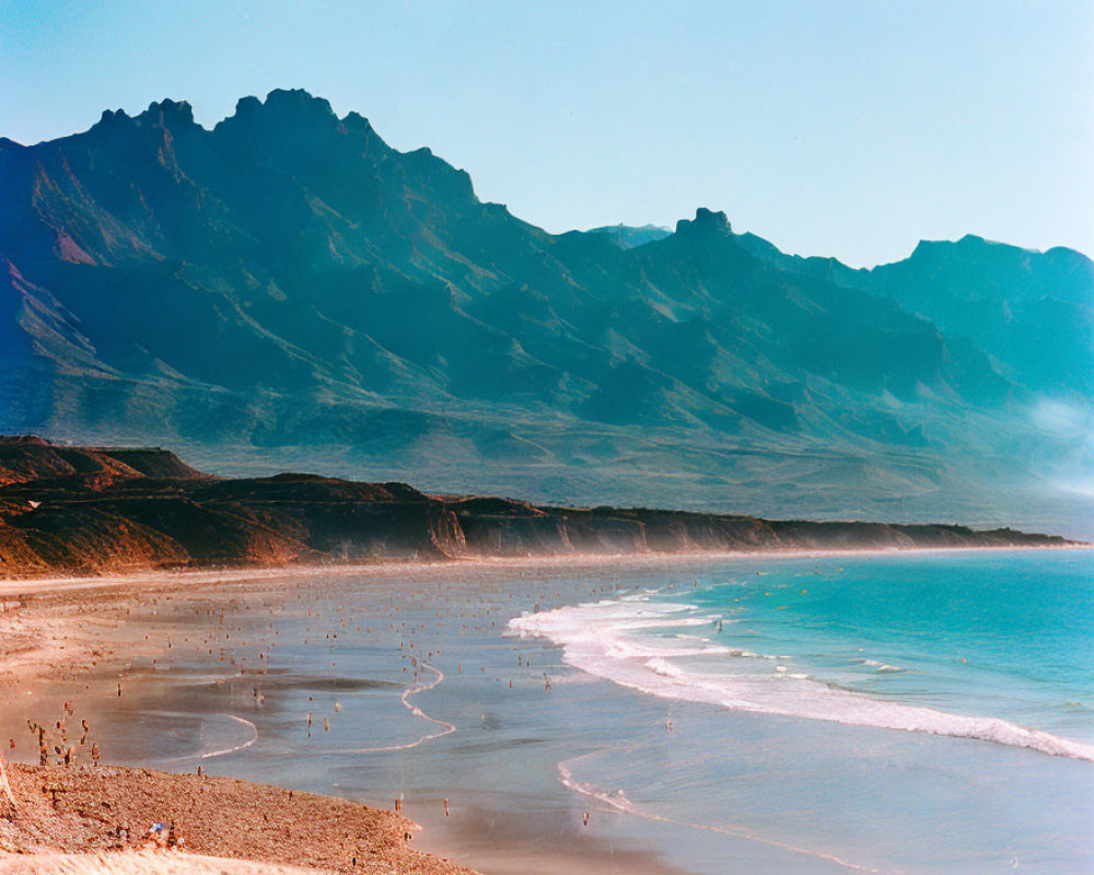Picturesque coastline with sandy beach, gentle waves, and majestic mountain range.
