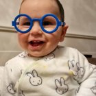 Baby in blue glasses holds doll with flower headband