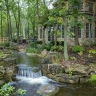 Tranquil stream with cascading water, lush forest, and quaint cottage.