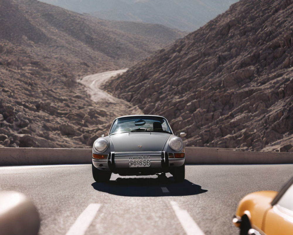Classic Cars Driving on Mountain Road with Clear Skies & Rugged Terrain