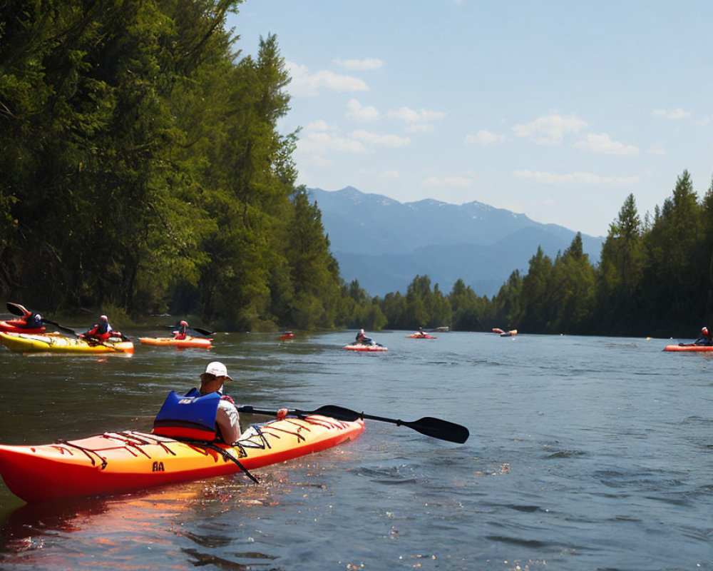 Kayakers on serene river with trees, mountains, and clear sky