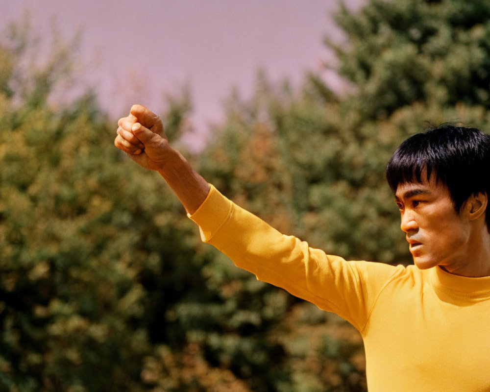 Confident man in yellow shirt practicing martial arts outdoors with trees in background