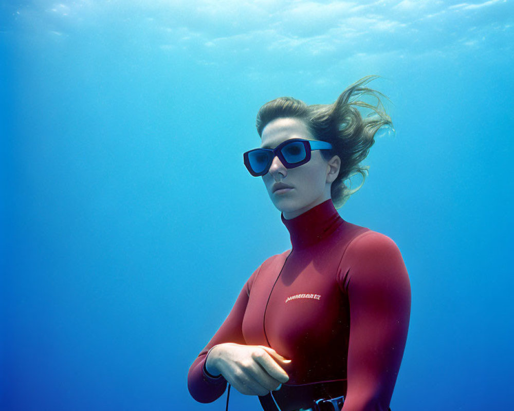 Woman in wetsuit and sunglasses underwater with flowing hair & clear blue water