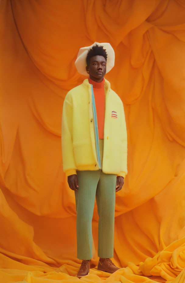 Person in Yellow Jacket, Green Trousers, White Hat Against Orange Backdrop
