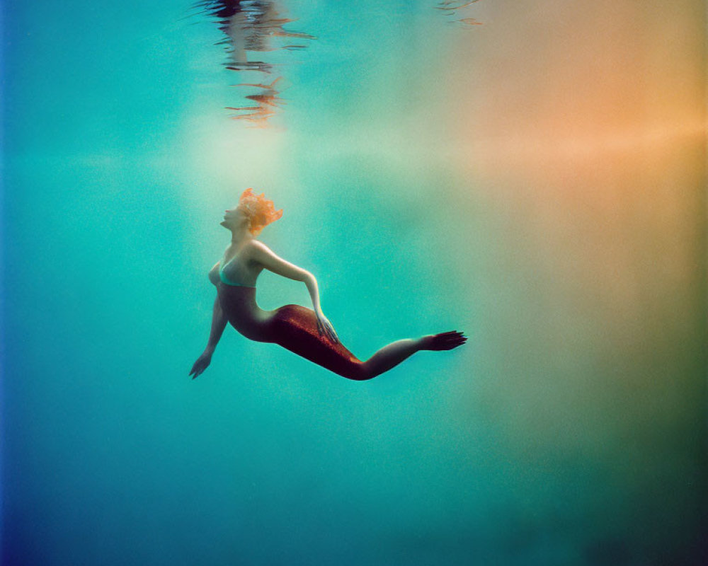Mermaid-like figure with red tail underwater in surreal lighting