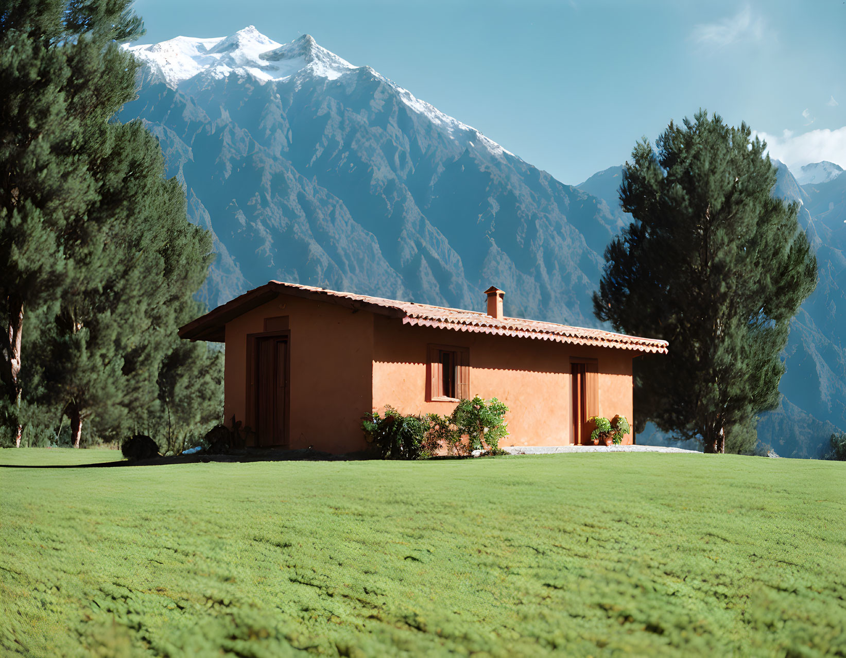 Tranquil landscape with brown house, green lawn, mountains, blue sky