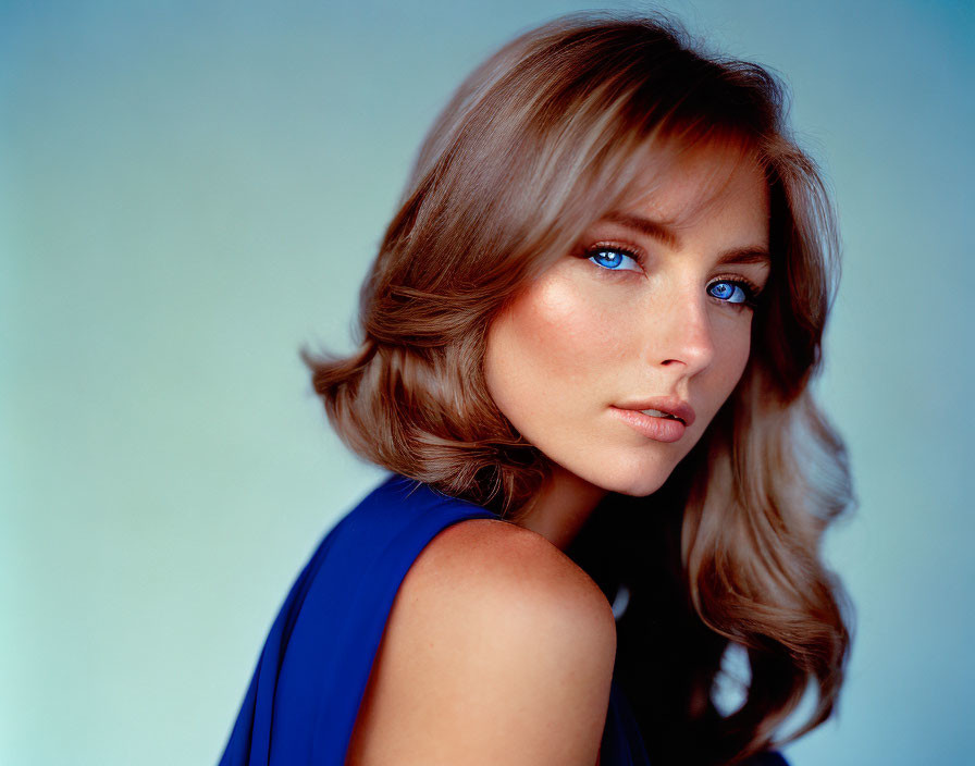 Blue-eyed woman with brown hair in blue top on soft blue background