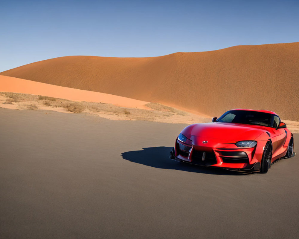 Red sports car parked in vast desert landscape with smooth sand dunes under clear blue sky