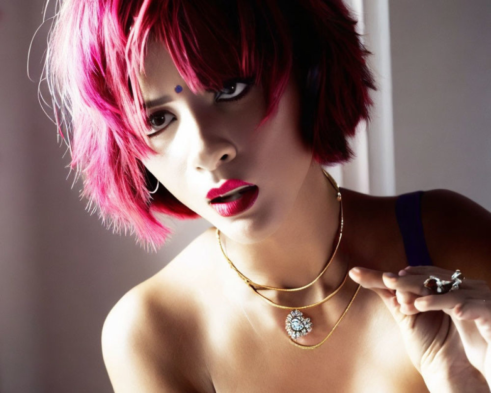 Vibrant woman with pink hair and bold makeup holding an object in gold necklace portrait.