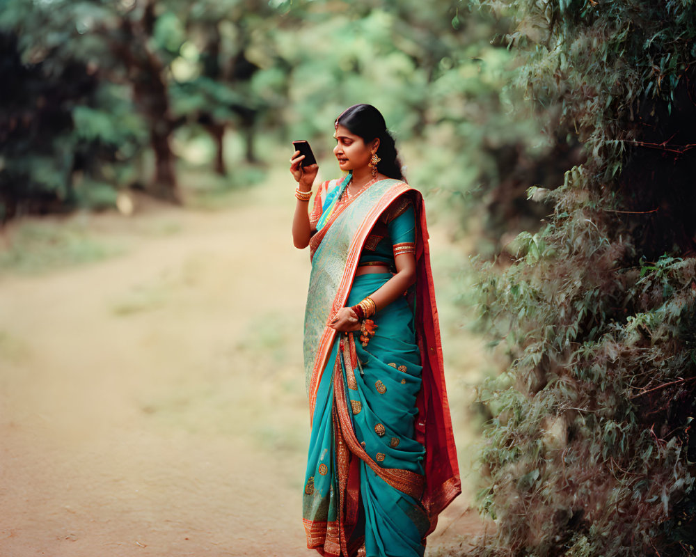 Woman in green and orange sari on dirt path with smartphone