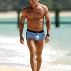 Fit man in metallic swim shorts strolling on sunny beach shore