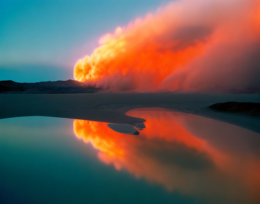 Fiery orange clouds reflected in calm water with dark dunes